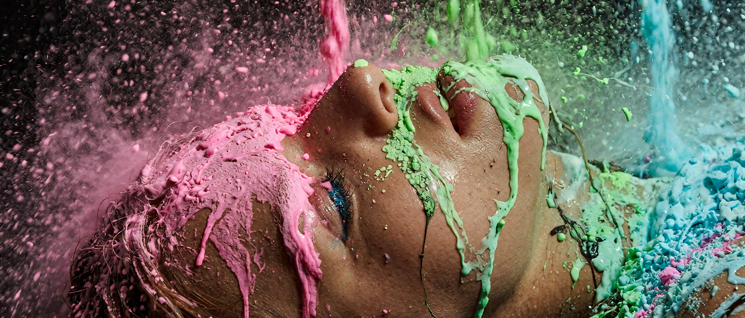 Pink, green and cyan pigment cascading over a face