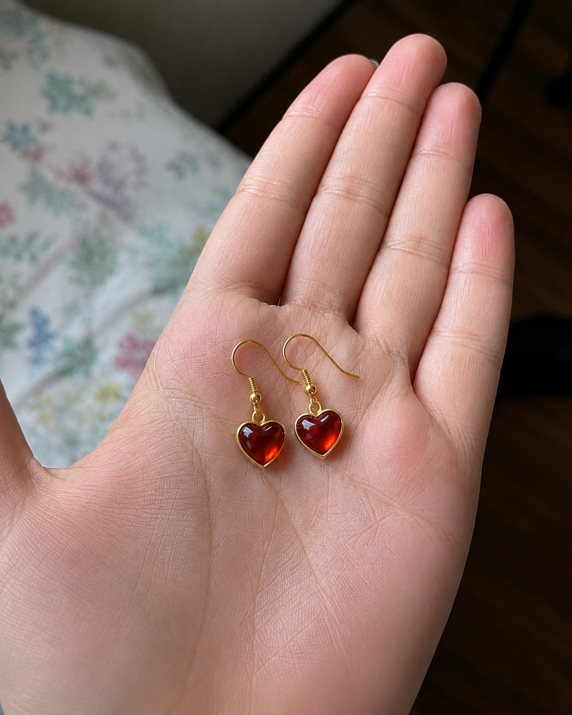 Reference photo: red glass heart earrings held in a hand